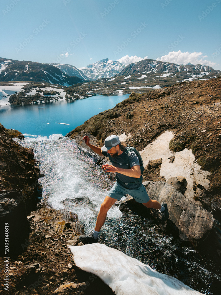 Fototapeta premium Man hiking solo in Norway travel trail running adventure in the great outdoors - active hiker traveler crossing river in Lahko park, healthy lifestyle summer vacations endurance energy freedom concept