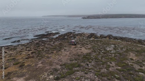 Drone shot of a vehicle along rocky coastal terrain with ocean backdrop in the Falkland Islands. Descending aerial footage.