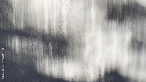 abstract monochrome light reflection shimmers along textured gray concrete wall casting ethereal dark shadow