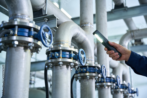 Schilderij op canvas Industrial inspection of complex pipe system with a flashlight by a worker