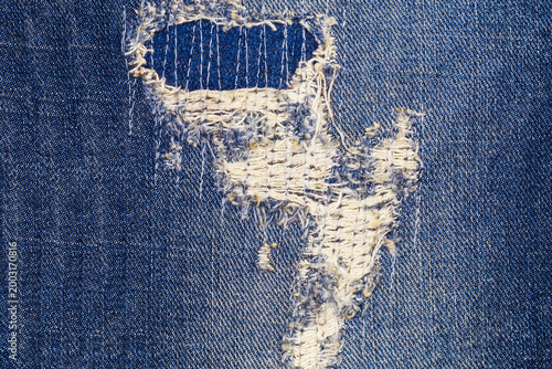 Fotografia Denim fabric shows wear with a hole and frayed edges in a piece of blue jeans