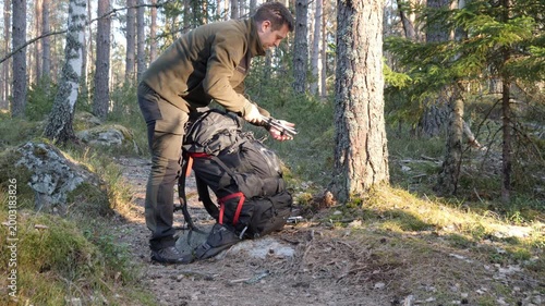 Man preparing backpack on forest trail during sunny outdoor hike