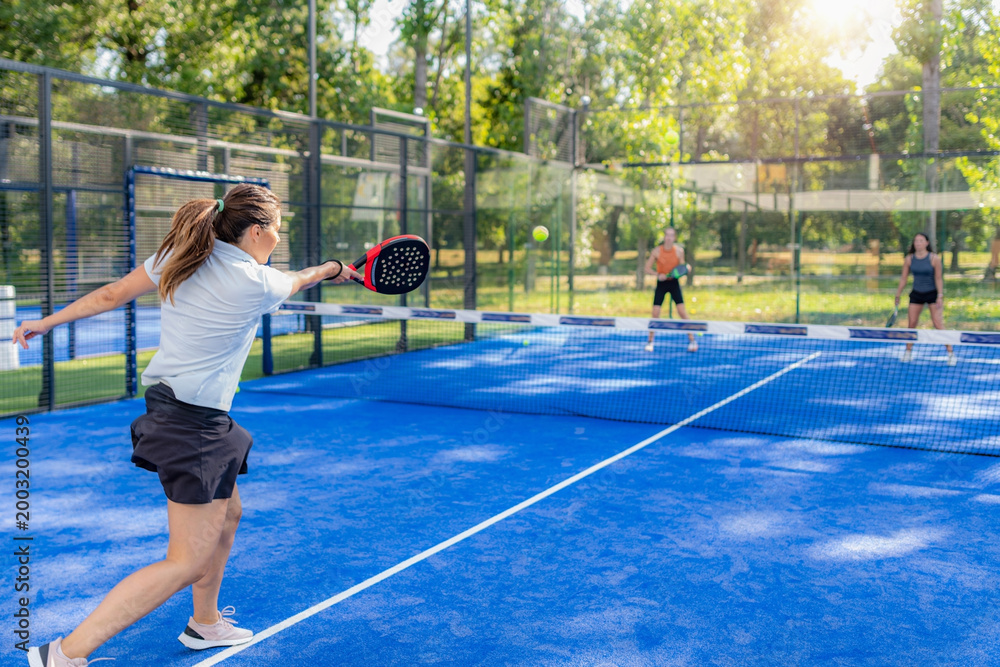 Obraz premium Padel player hitting forehand during outdoor doubles game, dynamic action with visible opponents and court environment.