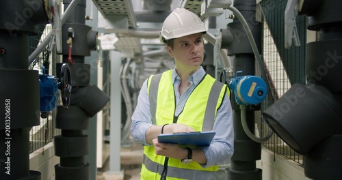 Quadro su tela A male engineer conducts a routine inspection of an industrial HVAC system in a plant room, checking machinery for performance and safety compliance