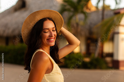 Fotografija Young woman in straw hat smiling with eyes closed at tropical resort