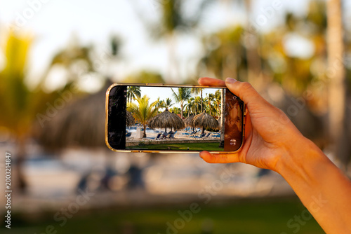 Konstfotografi Close up of hand holding smartphone capturing tropical resort scene