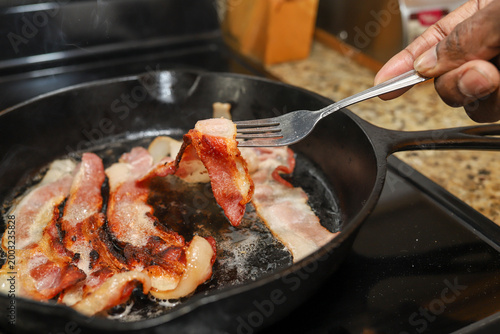 Schilderij op canvas Hickory smoked bacon cooking in a cast iron skillet in a home kitchen