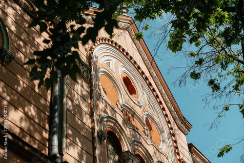 Historic townhouse facade framed by leafy trees in Subotica, Serbia. Ornate residential architecture in warm summer light.