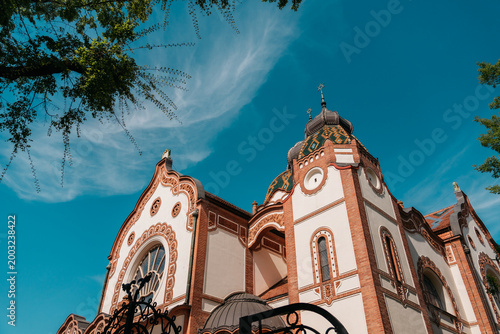 Decorative facade of Subotica Synagogue under vivid blue sky in Subotica, Serbia. Art Nouveau architecture with ornate brickwork and ceramic roof details.