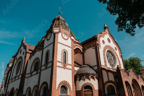 Decorative facade of Subotica Synagogue under vivid blue sky in Subotica, Serbia. Art Nouveau architecture with ornate brickwork and ceramic roof details.