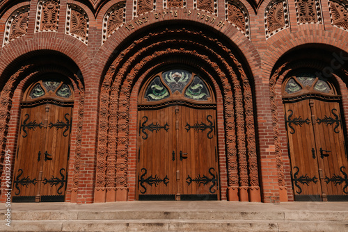 Ornate wooden entrance doors of Subotica Synagogue in Subotica, Serbia. Decorative brick arches and carved details highlight historic craftsmanship.