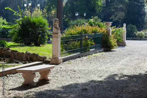 Classical stone bust and wooden bench in the tranquil gardens of Villa Borghese, Rome.