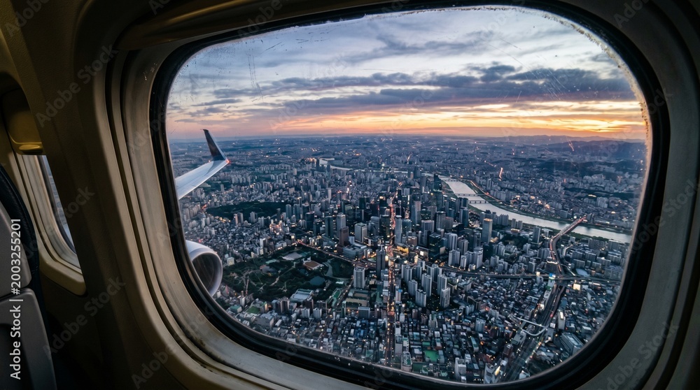 Fototapeta premium Aerial view of a sprawling cityscape at sunset, seen through an airplane window, with the sky painted in vibrant hues of orange and blue
