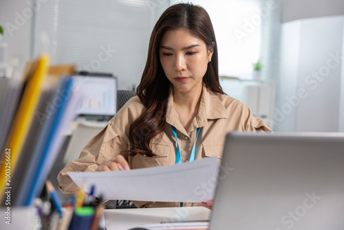 Tableau sur toile Serious young Asian business woman working at office desk reading document