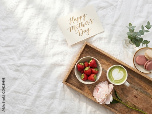 Mothers day breakfast in bed with strawberries, matcha latte, macarons, and a greeting card on a wooden tray