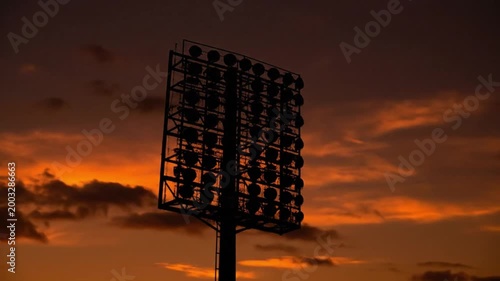 Silhouette of Stadium Floodlight Tower Against Orange Sunset Sky in Dramatic Sports Arena Timelapse