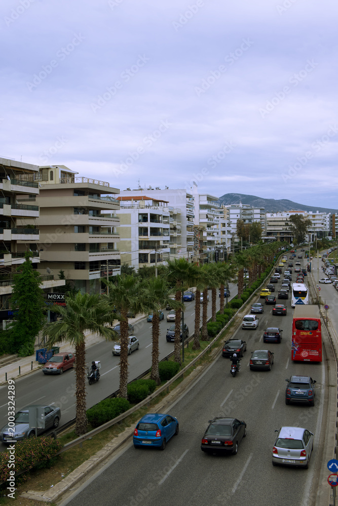Obraz premium Urban street with palm trees and active traffic, cars and public transport moving along a multi-lane road. Modern residential buildings and hills in the background. Concept of city life, transportatio