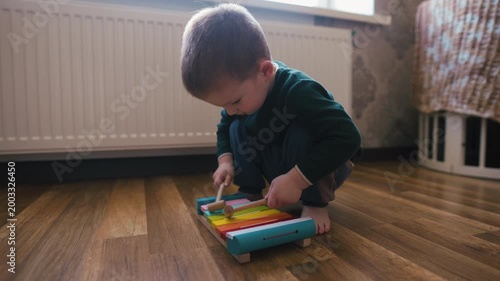 Little boy playing a colorful wooden xylophone on the floor at home, audio included