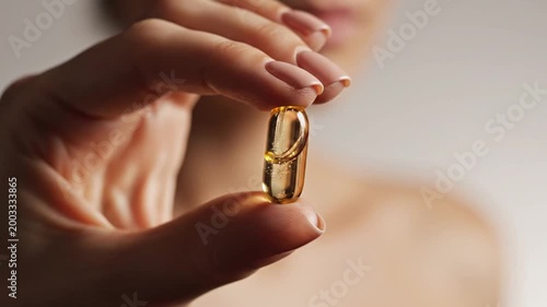 Woman holding golden health supplement capsule.