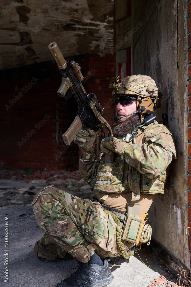 Obraz premium Armed Tactical Soldier In Camouflage Gear With Rifle Taking Cover In Urban Ruins