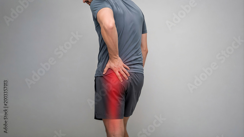 Photorealistic adult standing slightly sideways, one hand pressing the deep buttock/hip, mild discomfort suggesting piriformis syndrome with pain radiating to the posterior thigh.