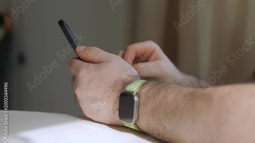 Hands use phone. Wristwear visible. White surface nearby. Indoor lighting. No animals or plants shown