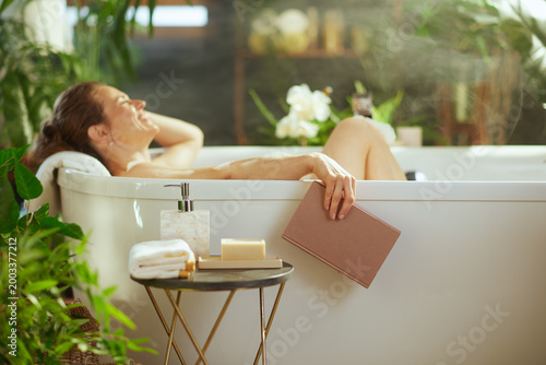 Bilde på lerret A smiling woman with brown hair enjoys a peaceful bath, reading a book on a soft towel