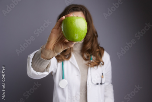 A female doctor holds a green apple to emphasize the link between diet and health. A creative shot perfect for nutritionists, dietitians, and wellness campaigns.