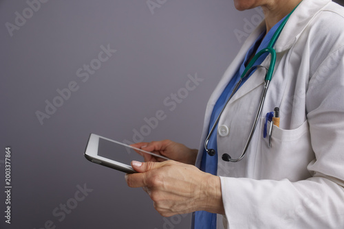 Close-up of a healthcare professional in a lab coat and scrubs using a tablet computer to manage patient records or conduct a telemedicine consultation.