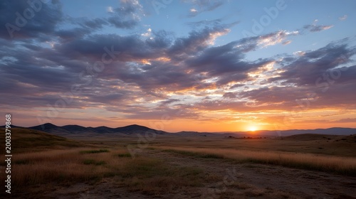 A breathtaking view of vast open fields beneath a dramatic expanse of colorful sunrise and sunset clouds over rolling hills