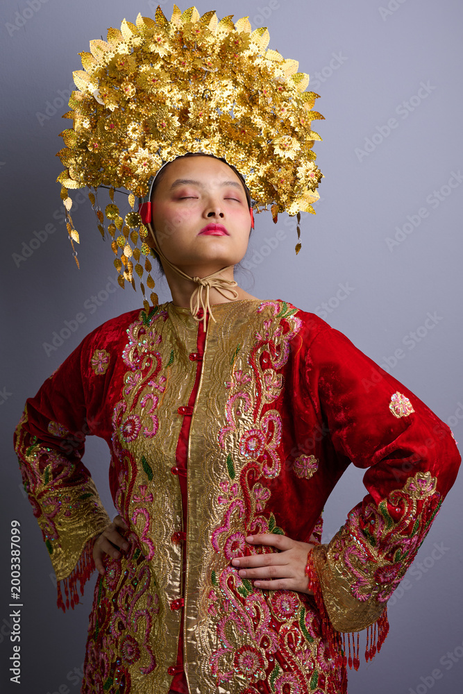 Obraz premium Portrait Of Indonesian Asian Woman Wearing Ornate Gold Headdress And Red Traditional Costume Celebrating Cultural Ceremony