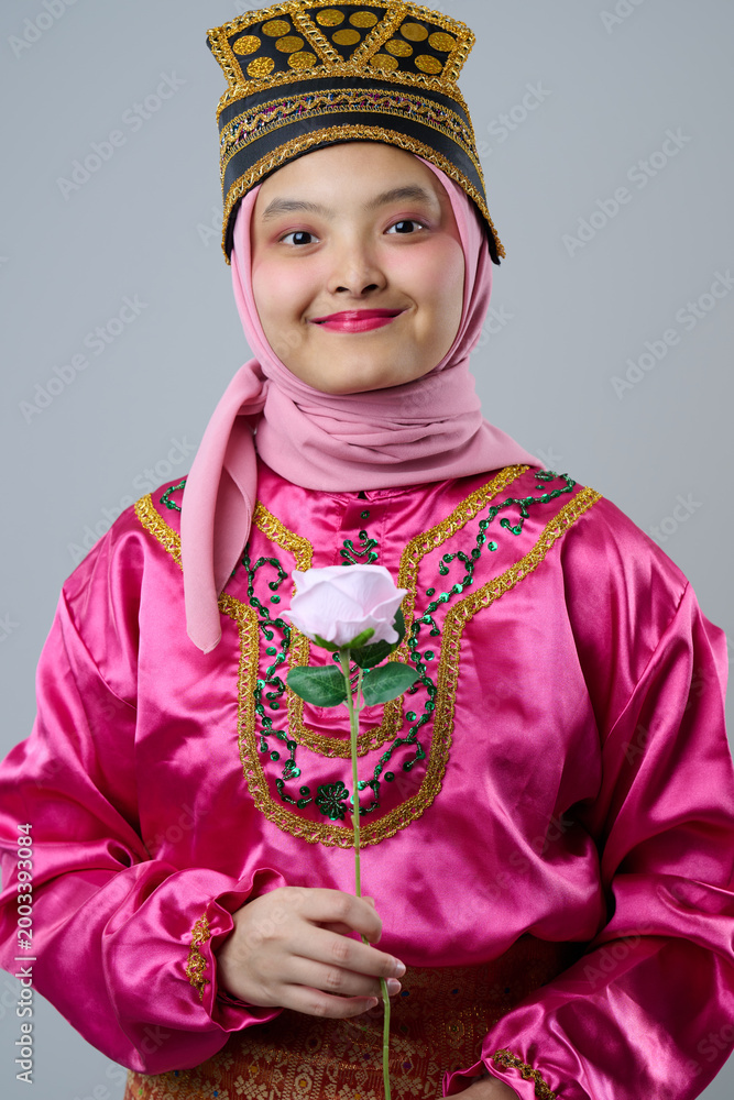 Fototapeta premium Smiling Young Indonesian Asian Girl Wearing Pink Hijab and Traditional Costume Holding a Rose Portrait