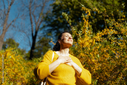 Surrounded by flowering shrubs and trees, a woman in a yellow sweater experiences the pure joy of spring. This portrait captures the essence of outdoor relaxation and happiness.