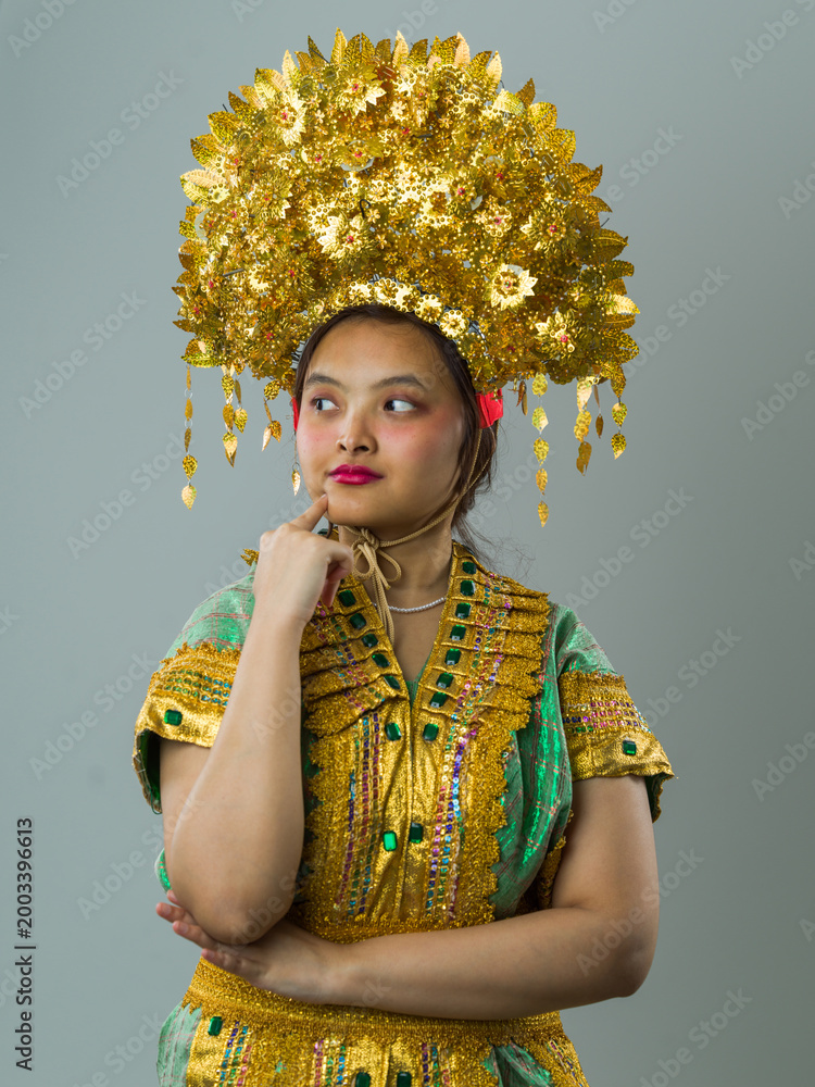 Fototapeta premium Portrait Of Young Indonesian Asian Woman Wearing Ornate Gold Headdress And Traditional Costume Expressing Thoughtful Confidence