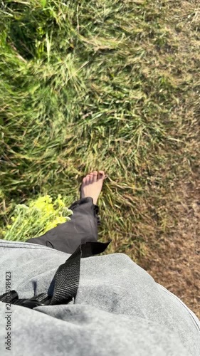 A woman's barefoot feet walk along a path of dry grass, holding a bouquet in her hands, viewed from above. Unity with nature, rest, relaxation, summer and natural scene