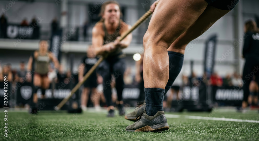 Fototapeta premium Muscular legs of athlete performing heavy rope sled pull on turf