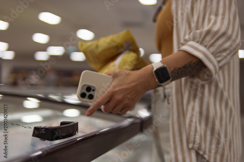 Canvas Print Woman shopping in supermarket, holding a smartphone and pointing at a frozen foo
