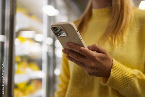 Foto Person checking shopping list on smartphone while standing near refrigerator in