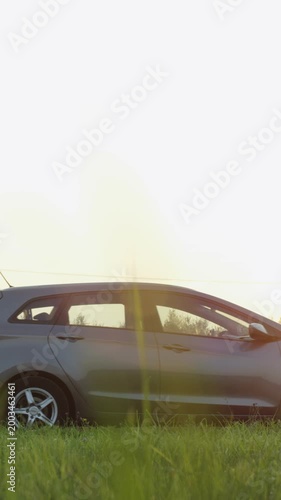 Man pushes his broken car down the road during sunset near a grassy area with trees and a clear sky in the background