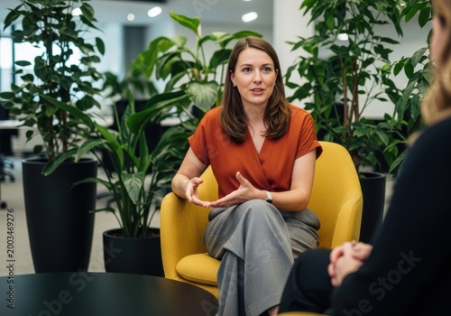 Professional woman in orange blouse sitting in yellow chair during meeting