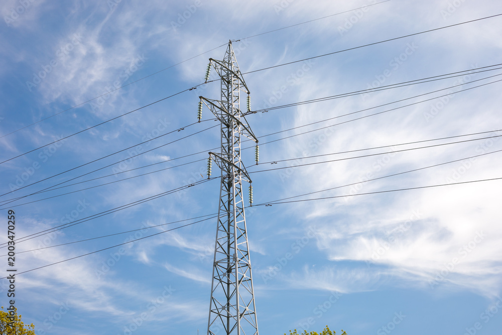 Obraz premium low angle view of a tall steel lattice electric power transmission pylon with ceramic insulators and multiple high voltage cables stretching across a partly cloudy blue sky