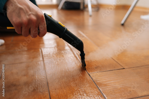 Cleaning service employee sanitizing floor with a steam machine, maintaining household cleanliness and effectively eliminating grime from tiled surface with hot steam. Concept of domestic hygiene.