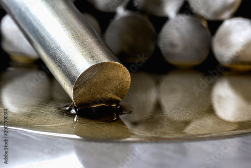 Close-up of steel rods arranged on a metal surface covered with machine oil, illustrating products of the metallurgical and chemical industry in an industrial environment.