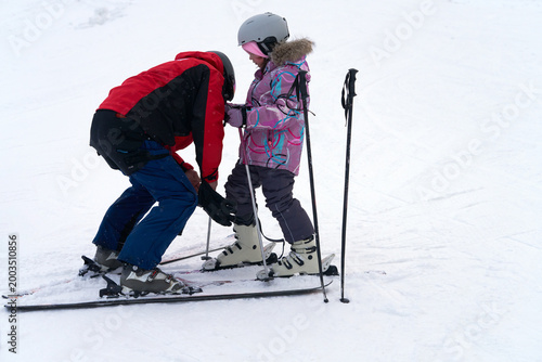 A children's mountain instructor adjusts the buckles on a boot to the size of a child's foot before training on the ski slope.