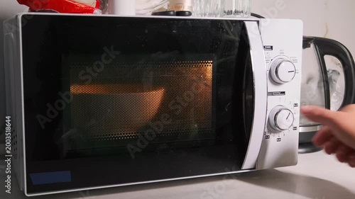 Close-up of a hand turning the rotary knob to start a microwave oven, setting cooking time and heating food in a modern kitchen appliance. Using microwave oven with rotary control