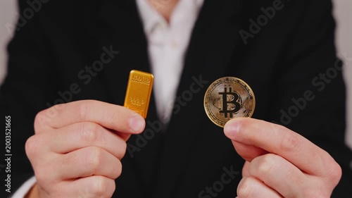 Une personne tient une pièce de Bitcoin et un lingot d'or dorée dans ses mains. En arrière plan, une personne en costume et chemise blanche. Concept de bitcoin vs or.
