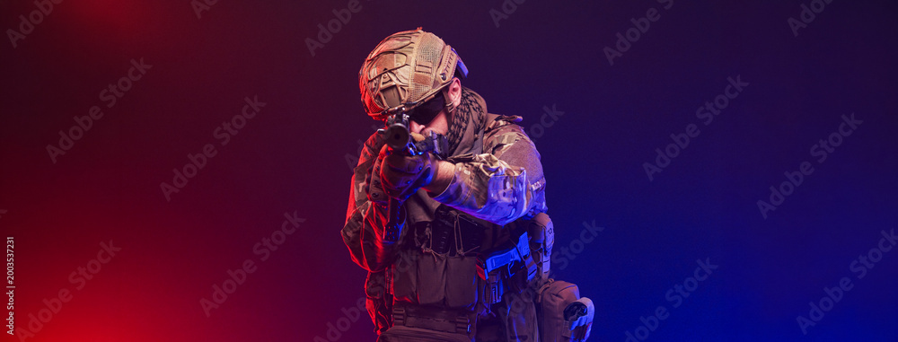 Fototapeta premium Tactical soldier on blurred red and blue studio background. Concept defense and modern warfare. 