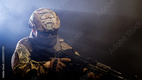 Bilde på lerret Soldier in tactical gear holding rifle on black background with smoke
