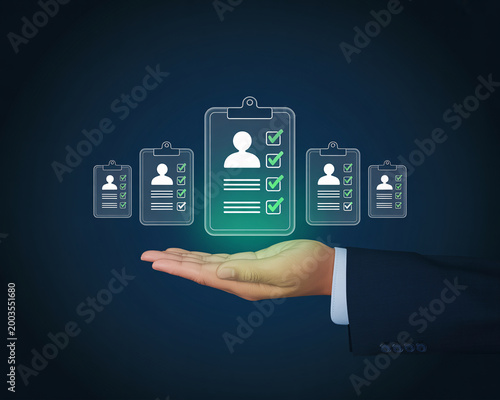A hand in a business suit holds a glowing green clipboard with a person's profile and checkmarks surrounded by smaller clipboards on a dark blue background