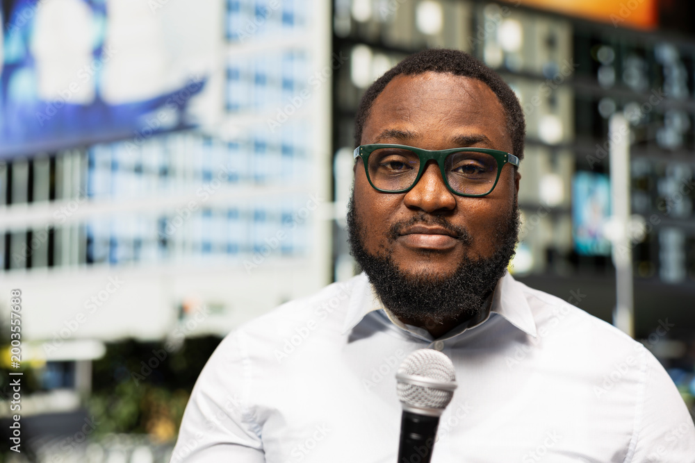 Obraz premium Close up of black adult reporter on busy city avenue holding microphone during a live interview, conveying news coverage and public information in modern metropolitan area. Field work.